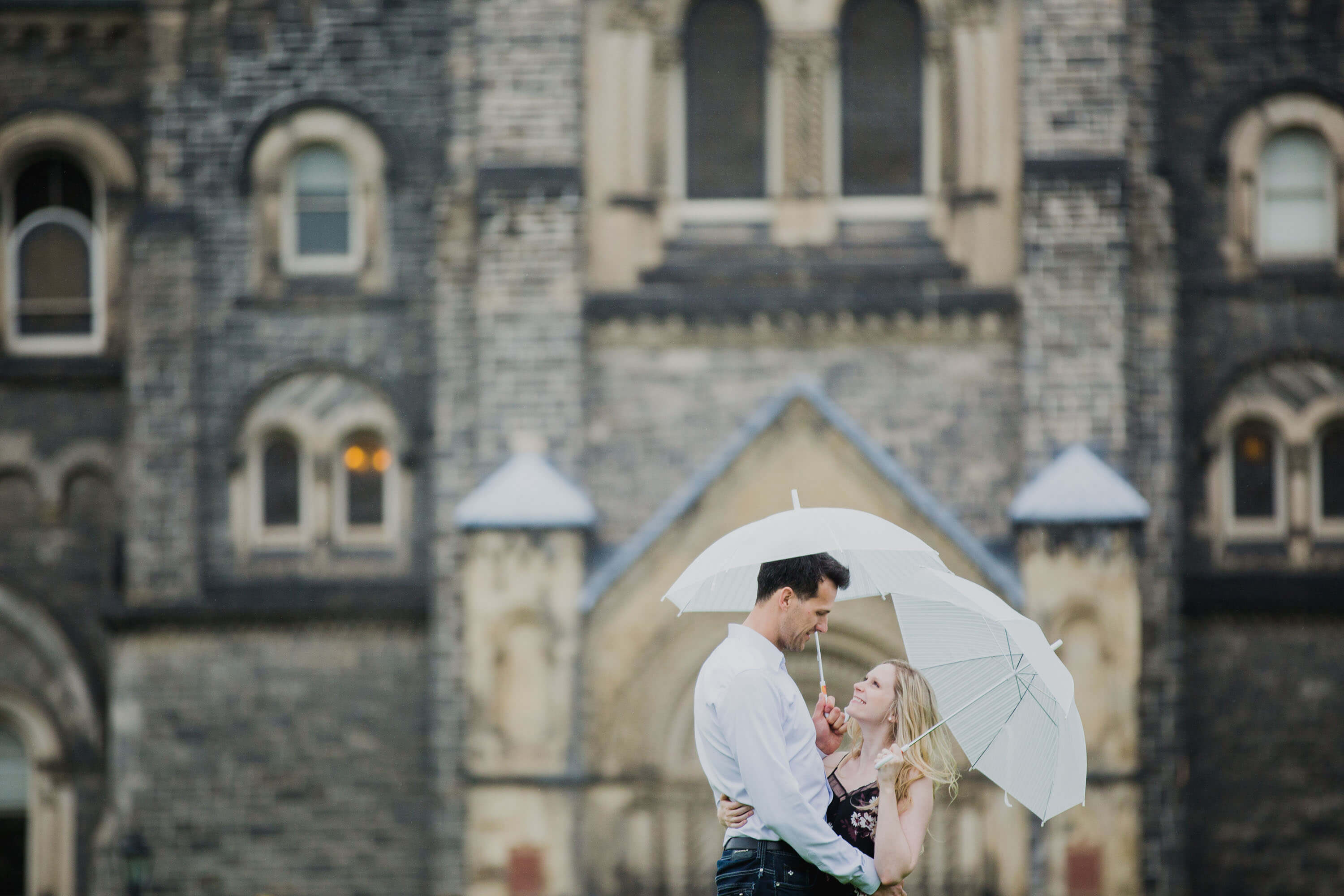 Toronto engagement session infront of stoney building. The couple poses with umbrellas to emphasize the beautiful rainy day