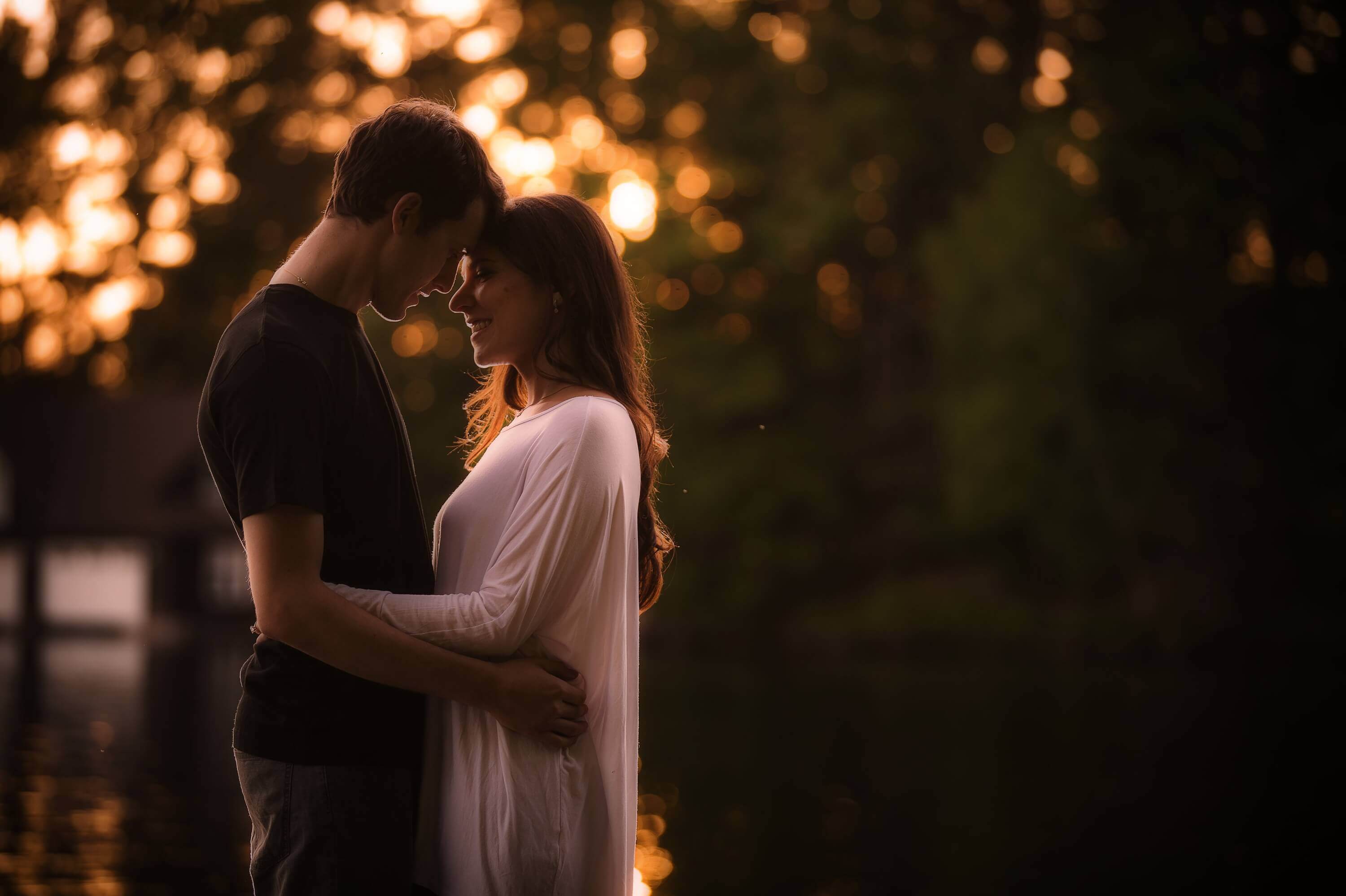 Couple posed with a natural forest and water backdrop, foreheads pressed together for an intimate glow at sunset