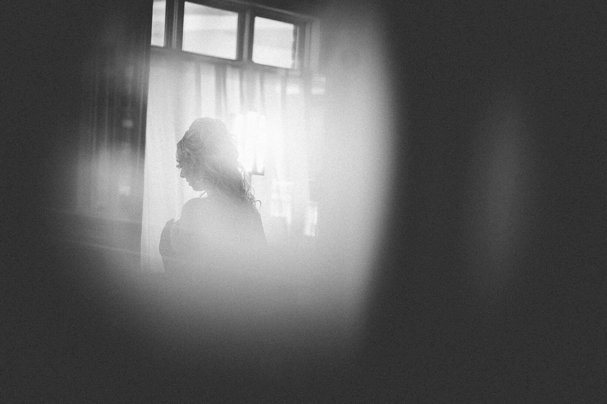 Black and white portrait of the Bride through a sheer as she gets ready at Lambton G&CC in Toronto