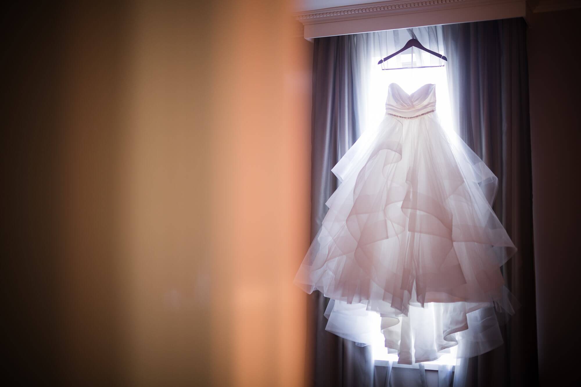 Beautiful detail shot of the dress hung in front of the window with a halo of light shining through