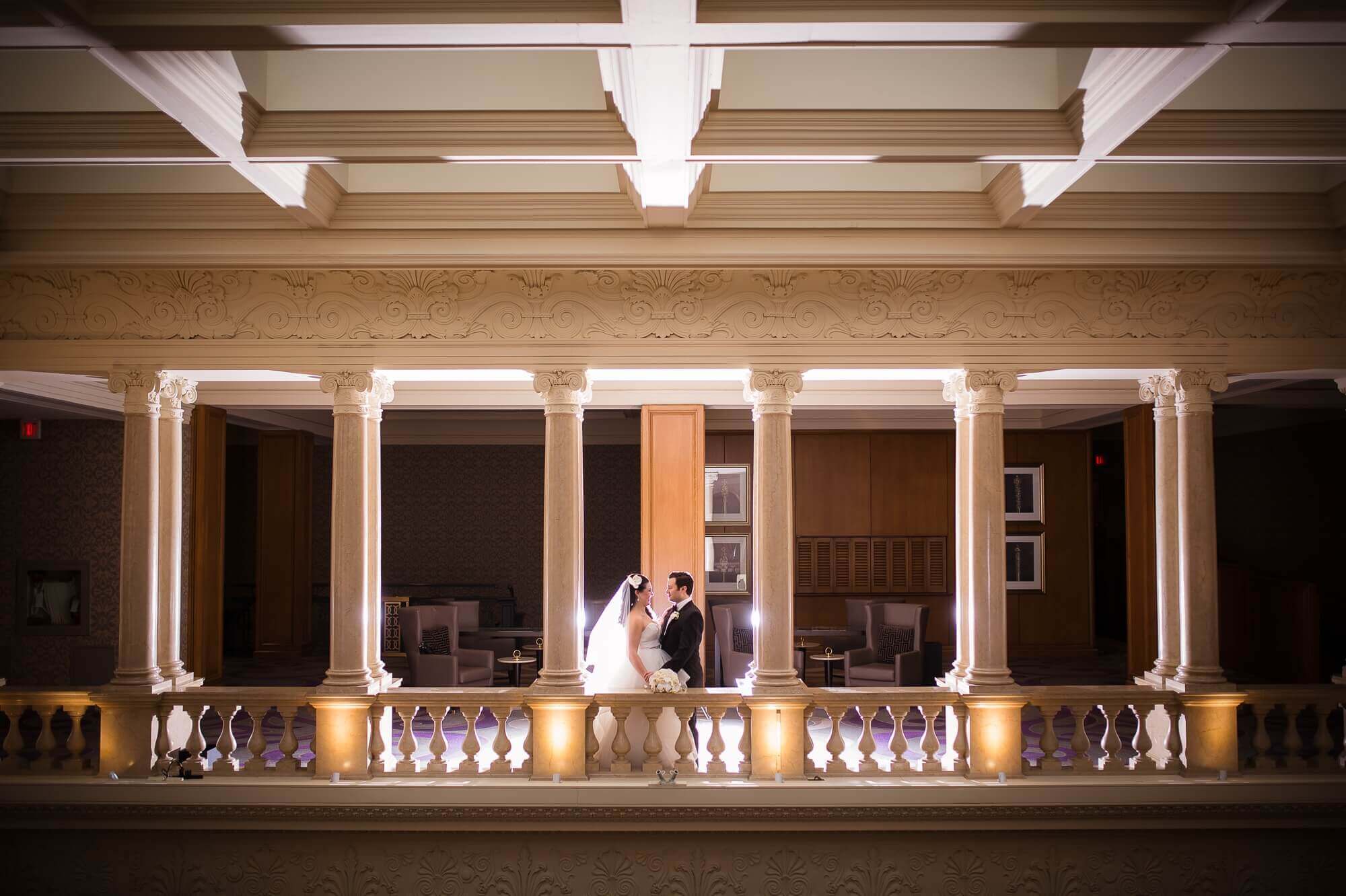 Beautiful architectural portrait of the bride and groom in between the columns at the Omni King Edward Hotel in Toronto