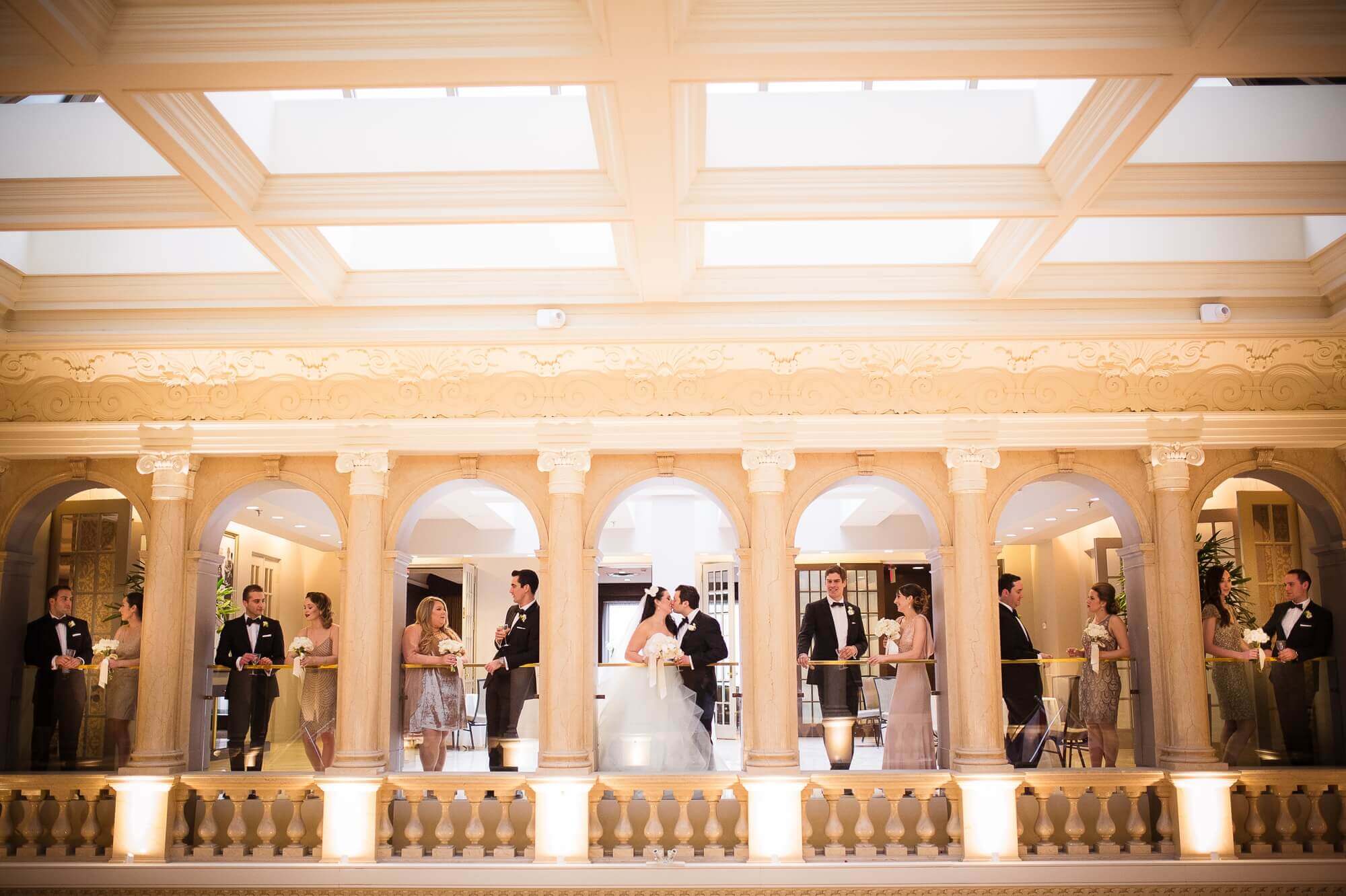 Portrait of the bride, groom and their wedding party, separated in between the columns at the Omni King Edward Hotel in Toronto