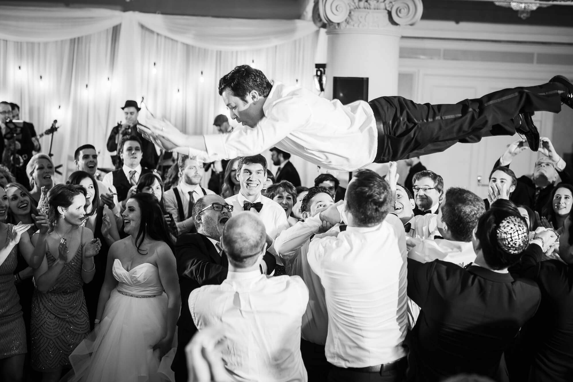black and white portrait of the groom being tossed in the air by guests at the Omni King Edward Hotel in Toronto
