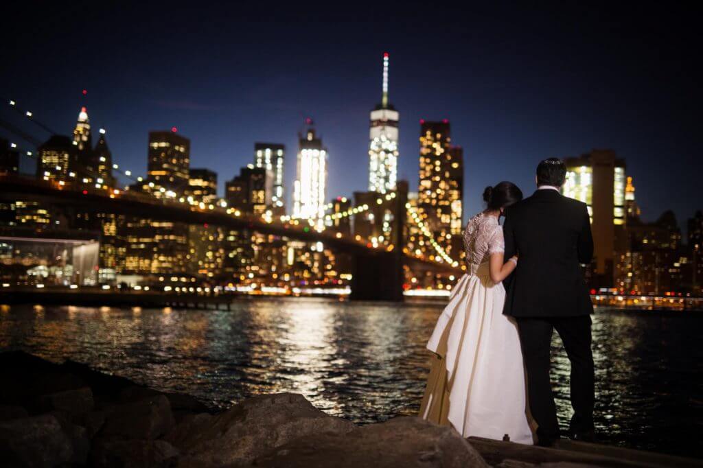 Jewish bride rests her head on her grooms shoulder as they overlook the city lights and bridge.