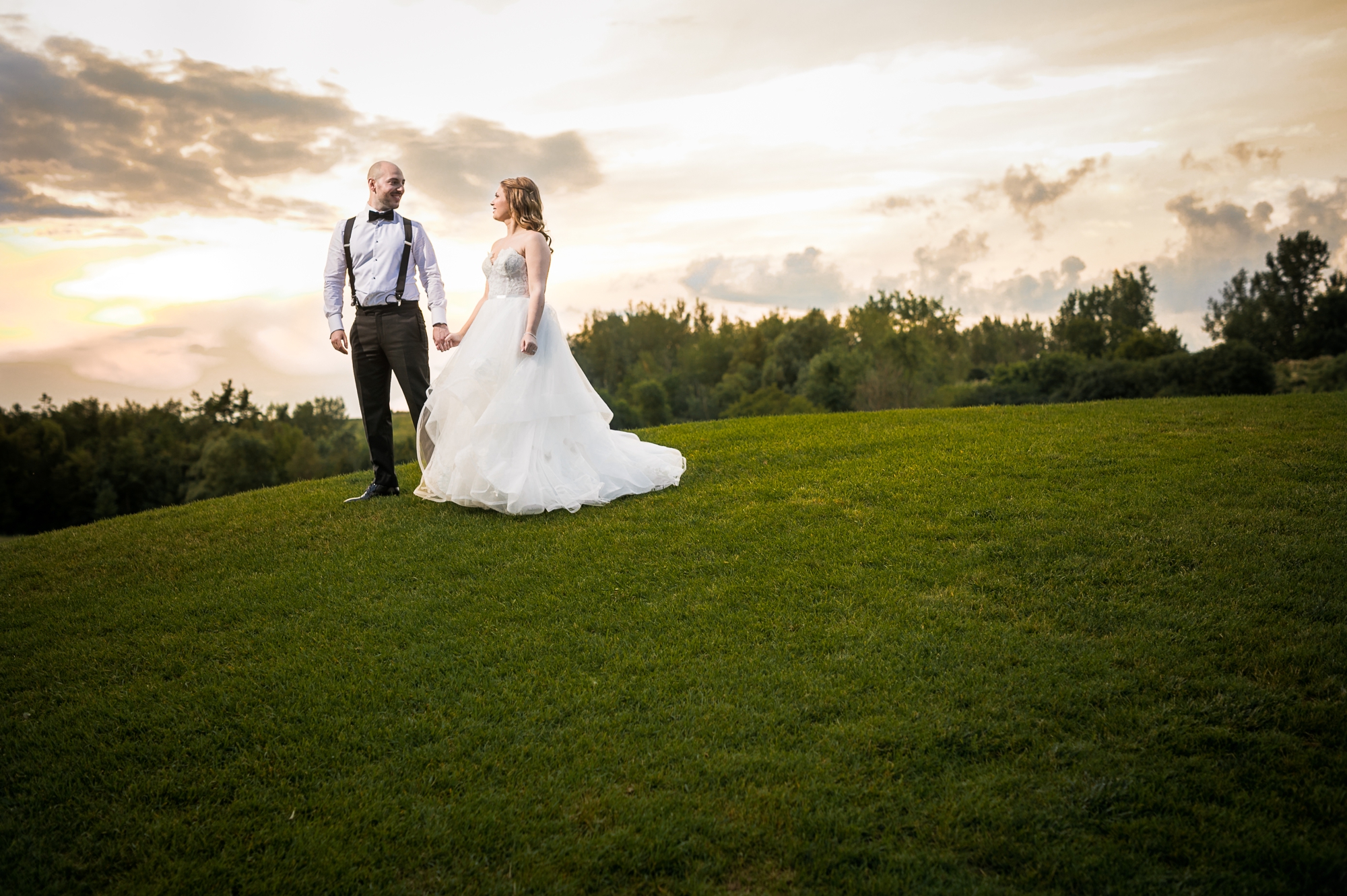 Bride and groom hold hands on top of a sunset hill.