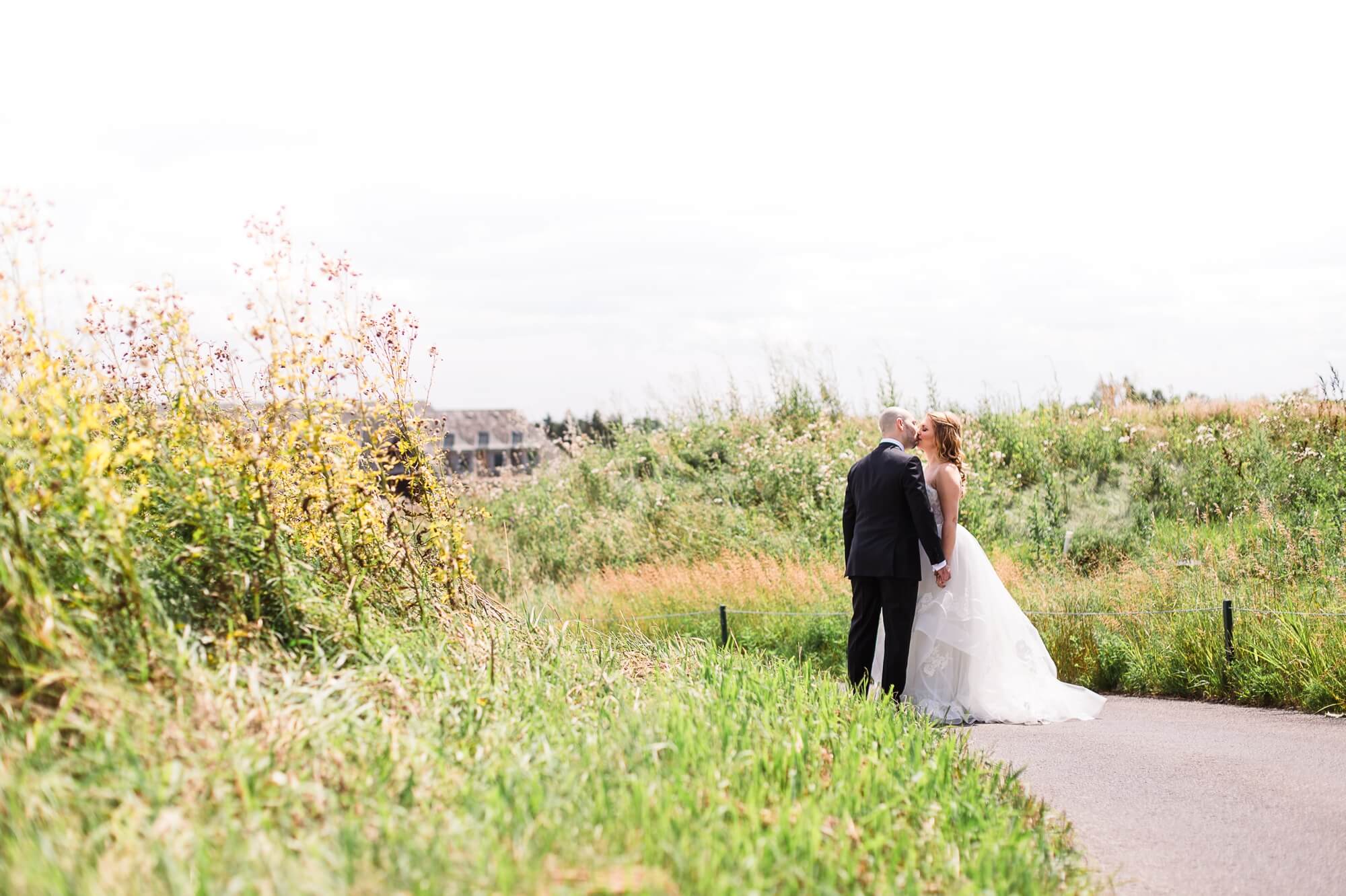 Toronto Wedding at Eagles Nest. Bride and groom kissing down a path surrounded by a beautiful overgrown green field.