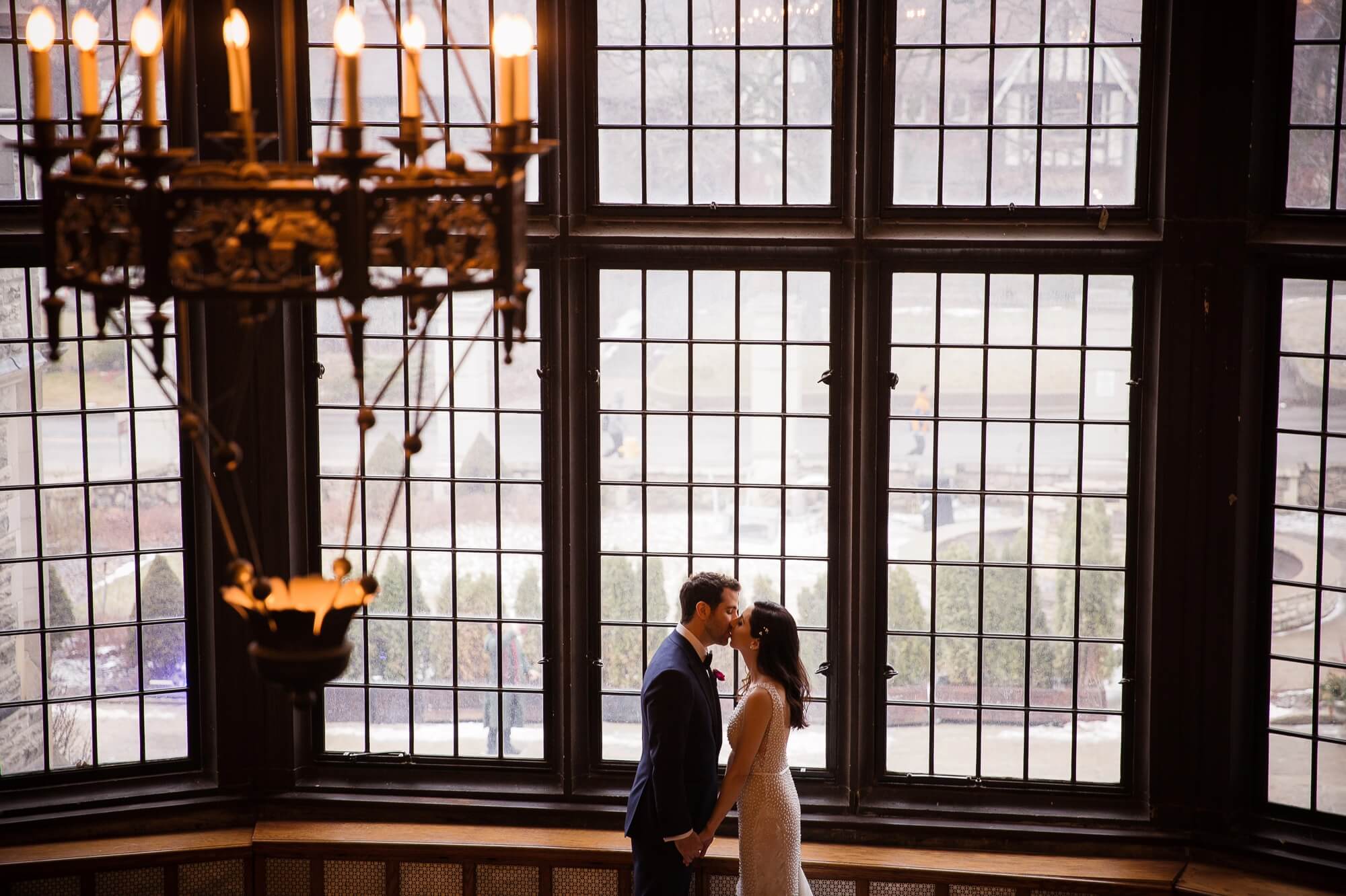 Dramatic Portrait of the Bride and Groom in front of a large window, under a candle chandelier at Casa Loma in Toronto